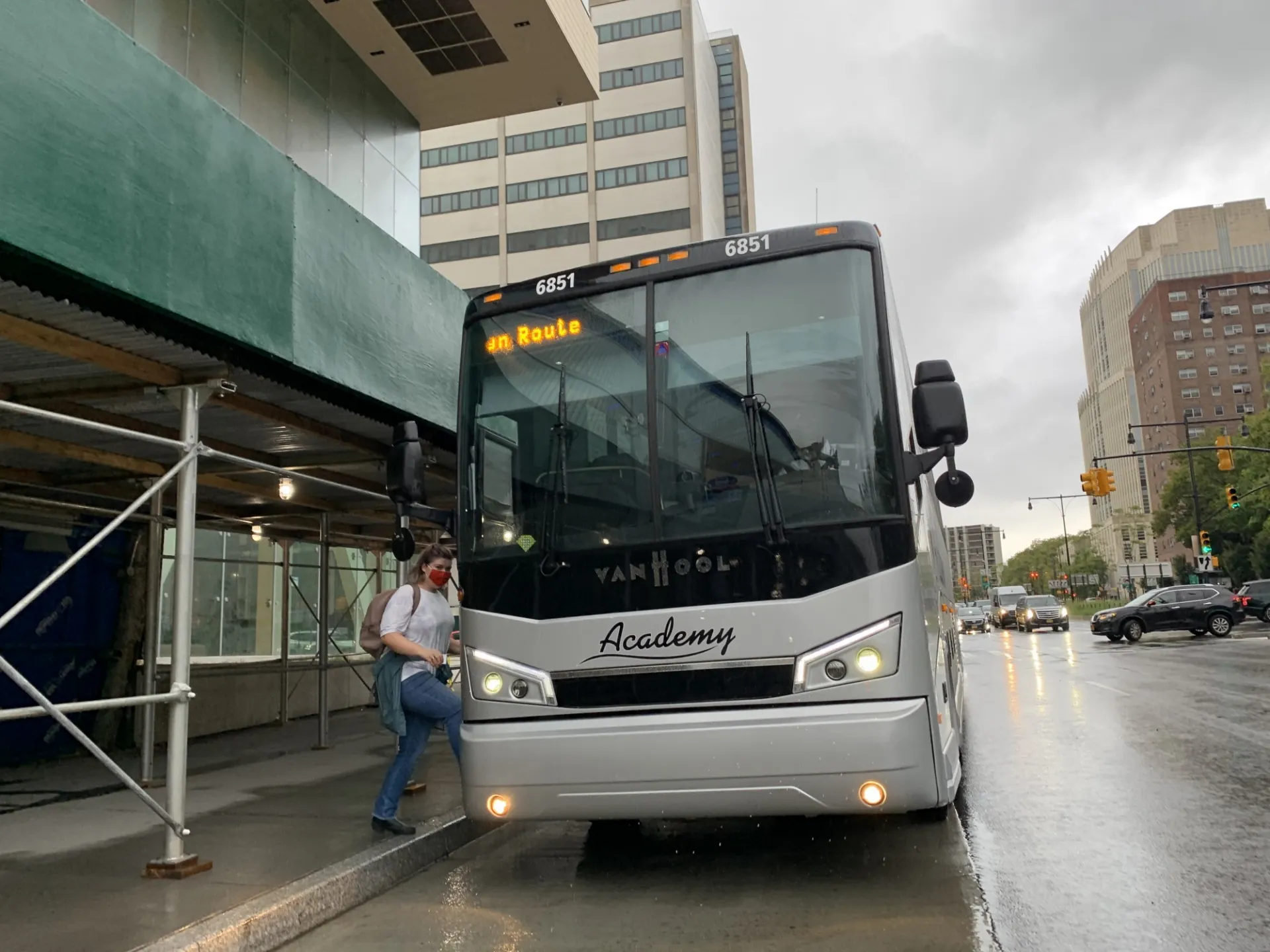 Passenger boards the Commuter Shuttle, wearing a face covering. The bus is branded with the Academy logo.