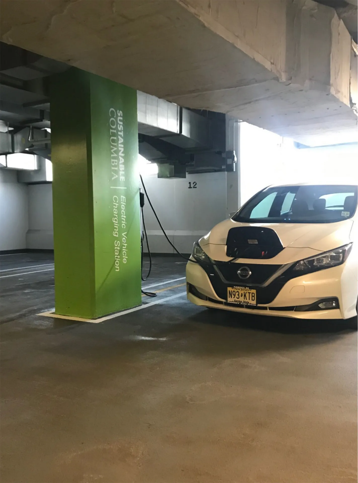 An electric car charging in the Columbia garage with the Sustainable Columbia green and logo on a pillar in the background.